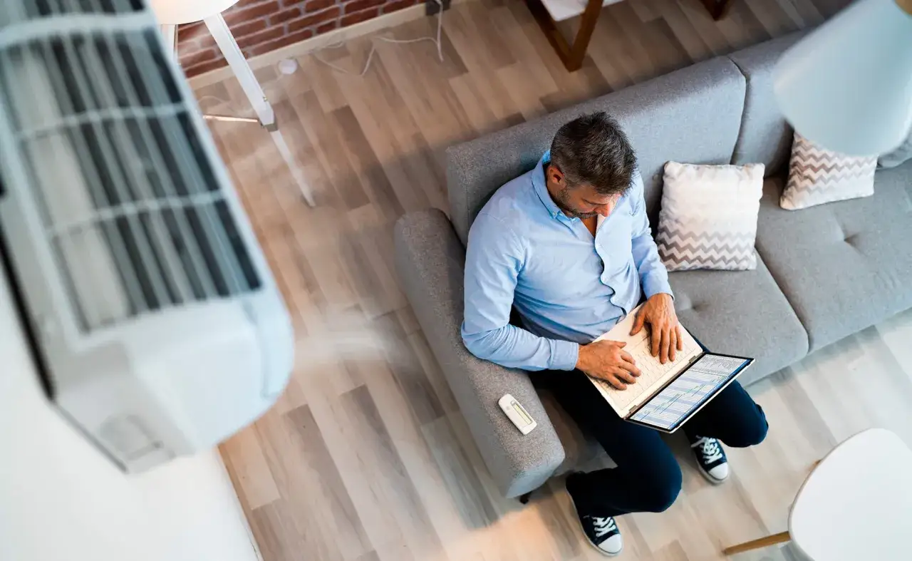 Hombre trabajando en portátil con aire acondicionado. Consejos para un uso eficiente y confortable.