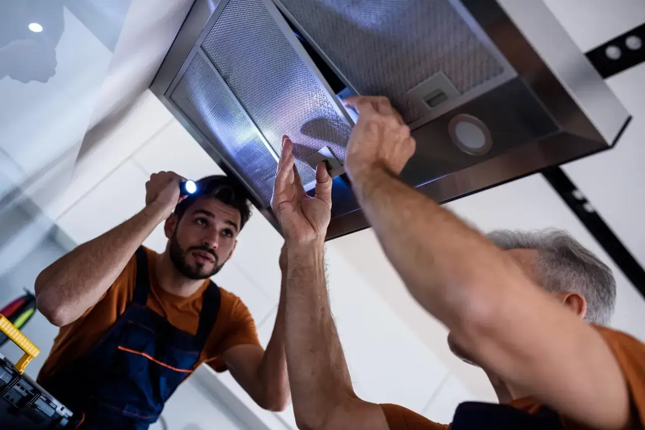 T&eacute;cnicos revisan campana extractora. Uno ilumina con linterna mientras el otro manipula el interior, buscando por qu&eacute; el motor no funciona.