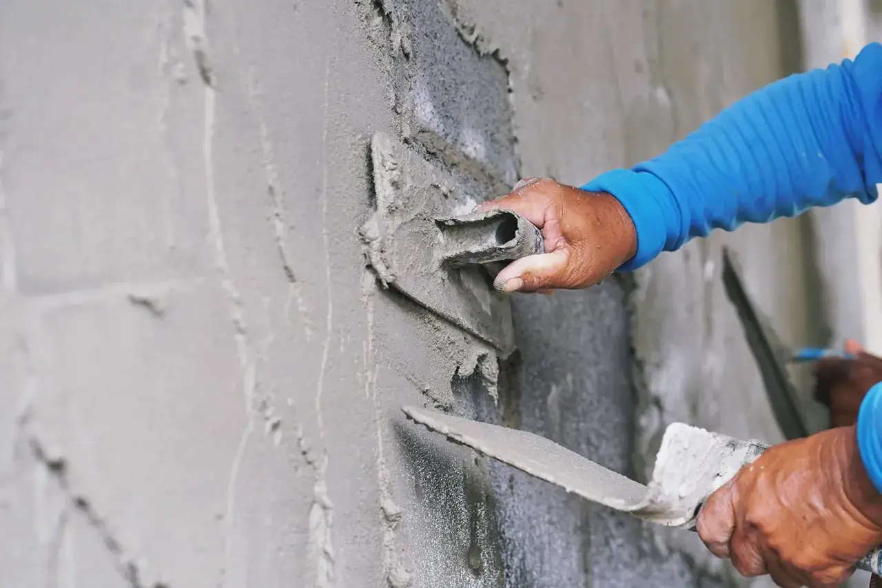Manos expertas aplicando mortero para reparar pared.