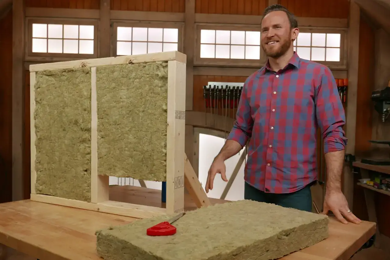 Hombre sonriente junto a un panel de aislamiento de lana de roca, mostrando su textura fibrosa. Se advierte sobre la lana de roca tóxica.