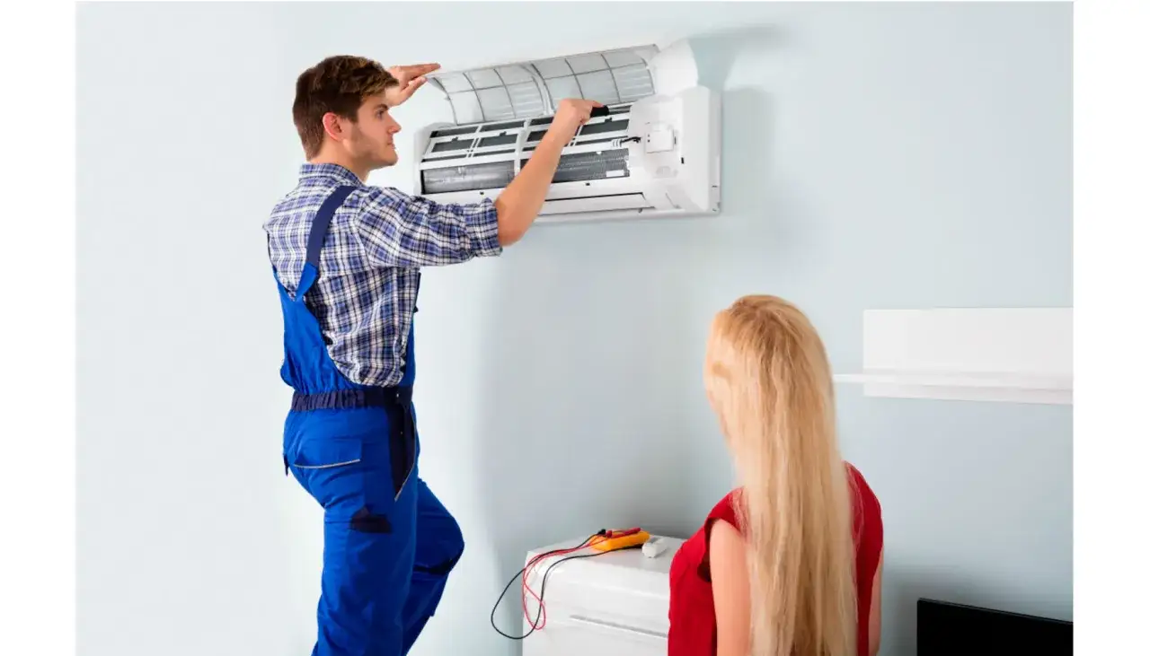 T&eacute;cnico realiza mantenimiento aire acondicionado split. Una mujer observa el proceso.