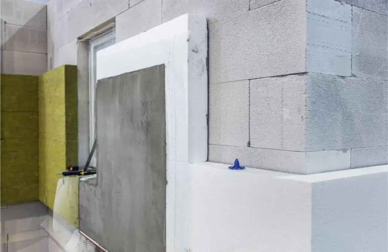 Construcción de fachada con materiales aislantes del calor: bloques de hormigón, lana de roca amarilla y poliestireno blanco.