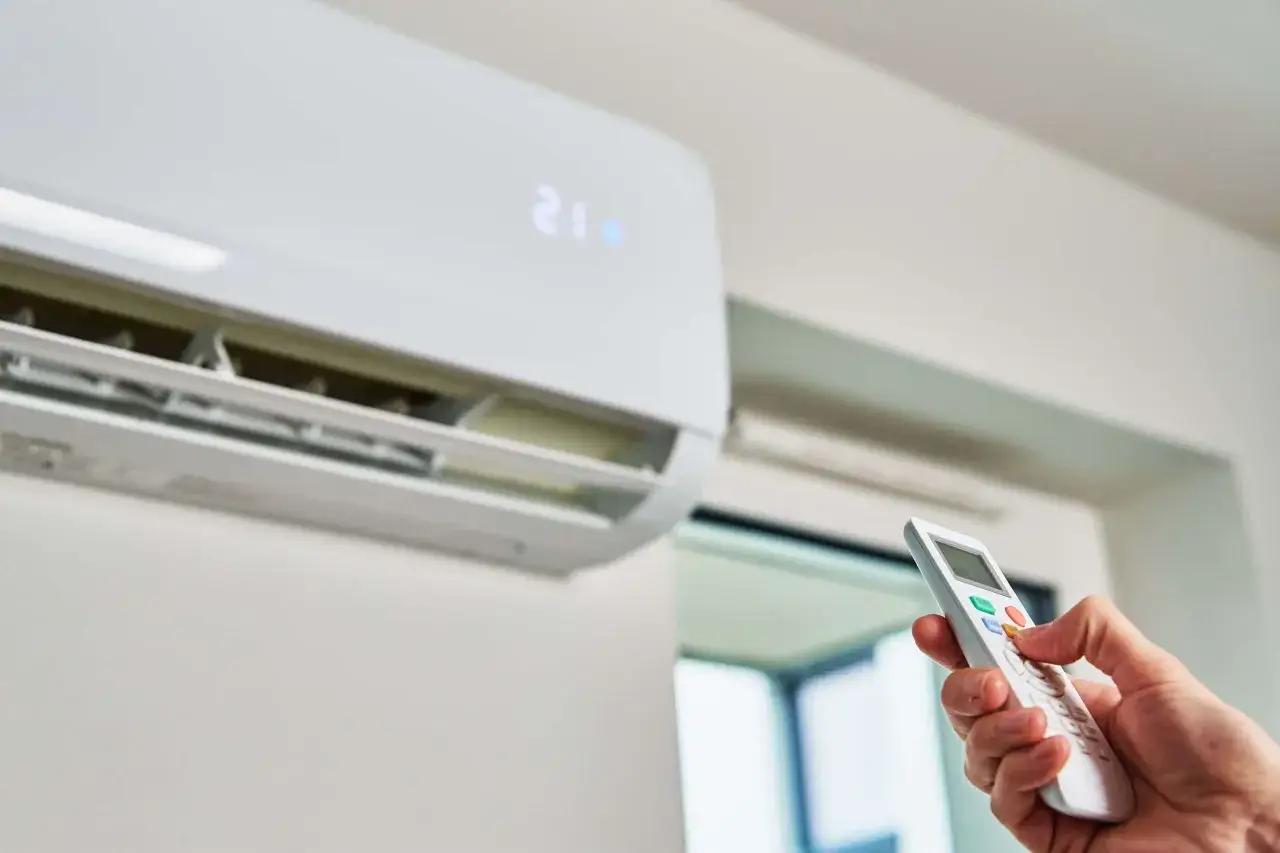 Mano ajustando el control remoto del aire acondicionado para que gasta menos. La pantalla muestra 21 grados.