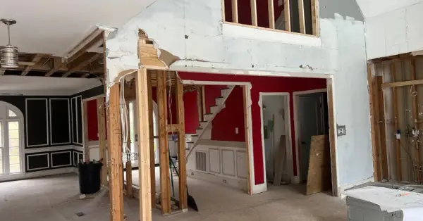 Interior en proceso de demolición, mostrando la estructura de madera expuesta y el cableado. Se observa una escalera roja y paredes parcialmente derribadas, como si se estuviera planeando como tirar una pared de casa.