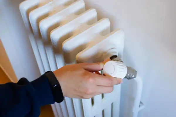 Mano ajustando el termostato de un radiador, parte de los contadores individuales de calefacción central.