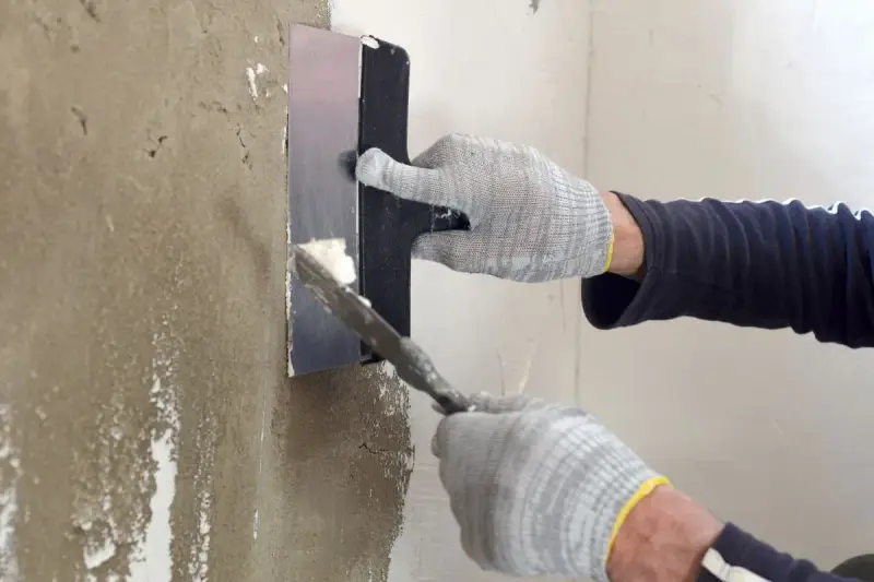 Manos enguantadas aplicando mortero para reparar pared.